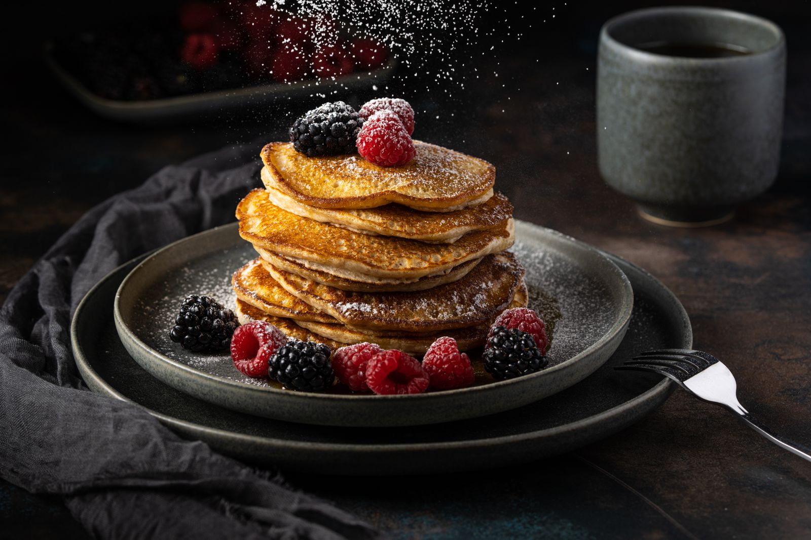 Stack of pancakes garnished with raspberries and blackberries, topped with sugar dusting.