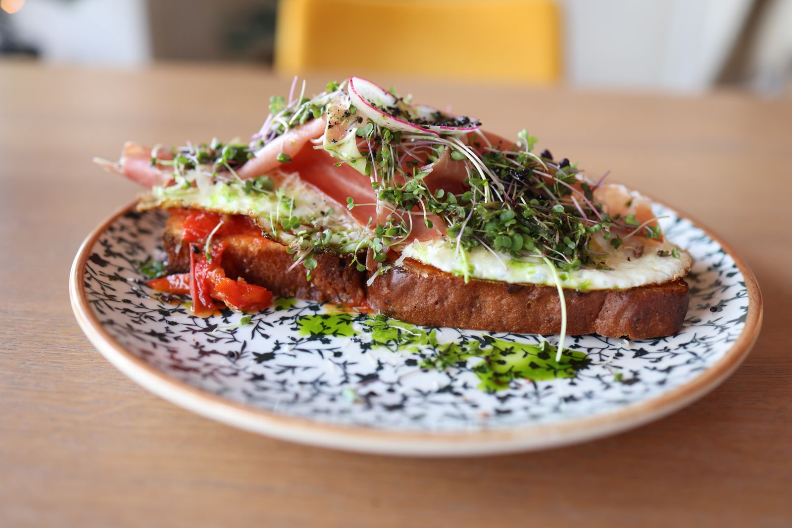 A gourmet open-faced sandwich topped with fresh greens and cured meat on a patterned plate.